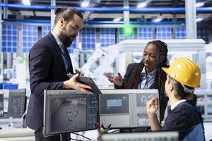 Solar panels plant manager showing employees factory energy consumption on tablet. Photovoltaics facility supervisor using device to present workers use of manufacturing resources photo