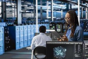 Data center programmer uses AI visualization tool on tablet to optimize resource allocation. Server hub IT professional uses artificial intelligence analysis on device to do maintenance photo