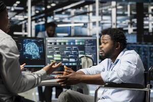 Engineer with disability and manager inspecting neural network data center used for machine learning. Team leader and worker in wheelchair optimizing server hub for artificial intelligence workloads photo