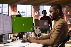 IT engineer using green screen PC in startup office and programming languages to build applications. Software development agency employee optimizing code on mockup computer photo