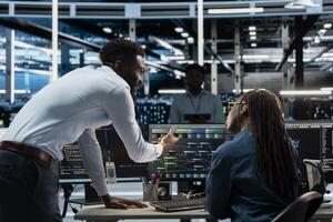 Server farm team leader overseeing work done by expert upgrading artificial intelligence systems. Data center manager supervising worker programming equipment used for machine learning training photo