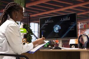 Woman in home office using financial application UI on PC screen showing company revenue and expenses. Accountant working from apartment doing annual profits review using computer photo