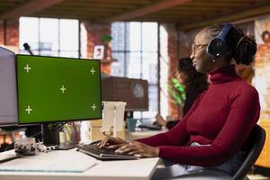 Programmer coding in startup office using isolated screen PC, listening music. African american AI industry startup technician wearing headphones using chroma key computer photo