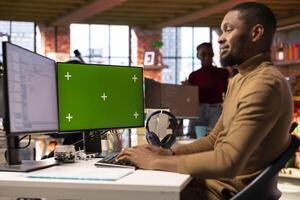 Smiling IT engineer using isolated screen PC in startup office and programming languages to build applications. Happy software development agency employee optimizing code on chroma key computer photo