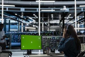 Servers room employee wearing audio headset doing maintenance using mockup PC. Technician in data center using green screen computer to check equipment performance, listening music photo