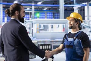 Smiling entrepreneur shaking hands with engineer in solar panel plant after reaching agreement for producing renewable energy. Businessman and worker in photovoltaics factory closing deal photo