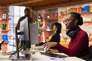 Programmer in startup office using large language model to get help with coding project. African american worker interacting with AI LLM chatbot PC GPT software on PC in software development workplace photo