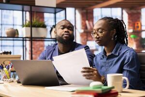 Black man and woman creating a report with information from papers and archived files, improving networking skills and achieving career independence. Remote workers solving tasks. photo