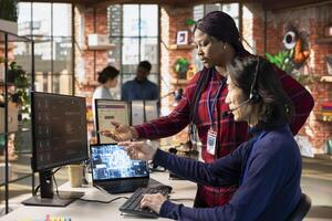 Call center supervisor guiding intern on how to use AI chatbot app on computer. African american customer support workplace onboarding specialist teaching man to use artificial intelligence software photo