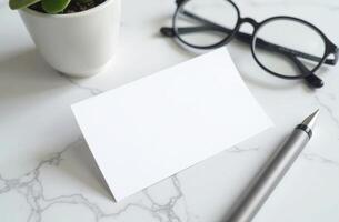A minimalist workspace featuring a blank card, glasses, a pen, and a small potted plant on a marble table photo