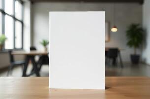 A blank notebook rests on a wooden table in a bright and minimalist workspace with greenery in the background photo