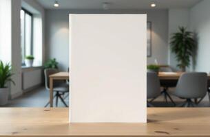 A blank book sits on a wooden table in a modern office with plants and a collaborative workspace in the background photo