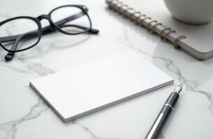 Blank business cards and stationery on a marble desk with a pen and glasses present a minimalistic workspace setup photo