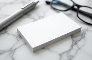 Blank business cards placed on a marble surface alongside a pen and reading glasses in a well-lit environment photo