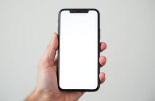 Hand holding a smartphone with a blank screen against a plain background in a well-lit setting photo