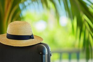 Straw hat resting on luggage against a backdrop of lush tropical greenery on a sunny day photo