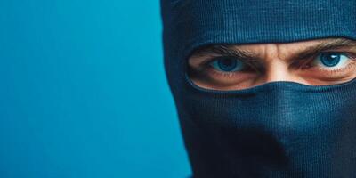 Masked individual with striking blue eyes posing against a simple blue backdrop during an intense moment of secrecy photo