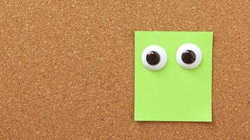 Fun and creative green sticky note with googly eyes on a corkboard background photo