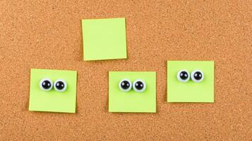 Creative arrangement of yellow sticky notes with googly eyes on a corkboard for fun decoration ideas photo