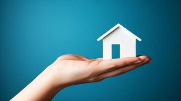 Miniature house held in hand against a blue background representing homeownership and real estate concepts photo