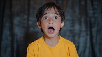 Child shows extreme surprise or fear in indoor setting with dark background while wearing a yellow shirt photo