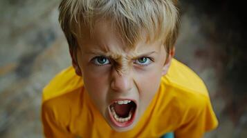 Young boy expressing intense anger in a bright yellow shirt in a natural indoor setting during daylight photo