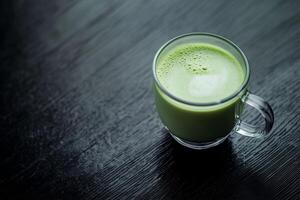 Freshly prepared matcha green tea served in a glass cup on a dark wooden table with a smooth surface photo