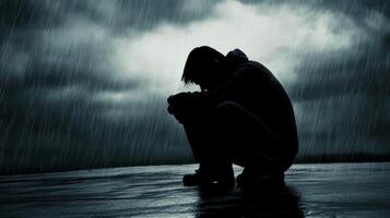 Man sits in the rain with head down, reflecting on personal struggles during a stormy evening photo