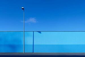 Vibrant blue wall under clear sky with streetlight casting shadow in urban area during daytime photo