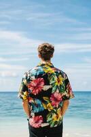 Man in tropical shirt enjoys a serene beach view as waves gently lap the shore under a bright sky photo