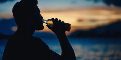Enjoying a refreshing drink at sunset by the water while silhouetted against a colorful sky photo
