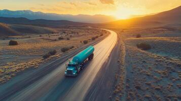 Long-haul truck travels along winding rural road at sunset with mountains in the distance photo