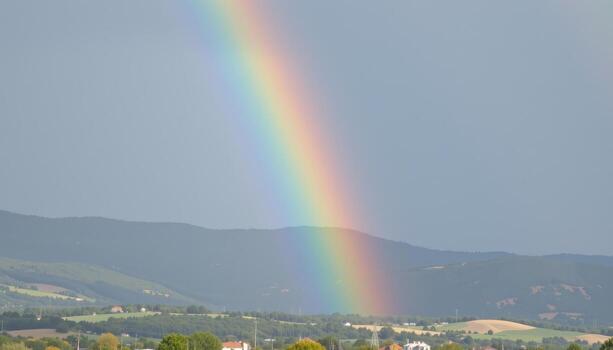 a faint rainbow appears above distant hills after a gentle afternoon rain. photo