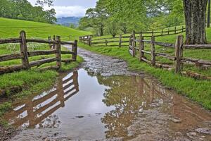 A muddy path leads to a wooden fence and a green field photo