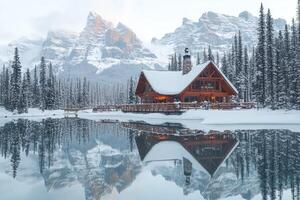 A cabin sits on the shore of a lake surrounded by snow covered mountains photo