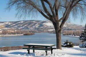 Snowy picnic table overlooking winter river and mountains photo