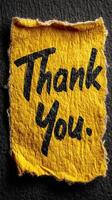 Bright yellow note expressing gratitude with handwritten thank you message on a textured black surface photo