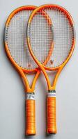 Tennis racquets in vibrant orange color with gray details resting on a neutral background photo