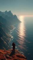 Mountainous coastline at sunset with a figure holding a spear overlooking the ocean photo