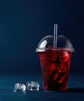 Refreshing red drink with ice in a clear cup against a dark blue background photo