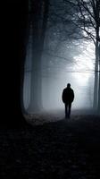 Silhouette of a lone figure walking through a foggy forest path at night photo