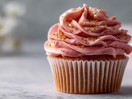 Delicious pink frosted cupcake with gold sprinkles on a marble tabletop photo