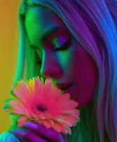 Woman sniffs pink gerbera daisy under neon light photo