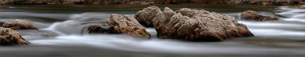 Smooth flowing water rushes around large rocks in mountain river photo