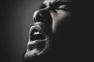 Man with dark hair screams in the darkness with open mouth photo
