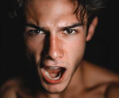Young man with intense expression screams in dark lighting photo