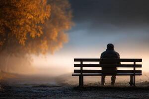 Man sits alone on park bench in autumn morning fog photo
