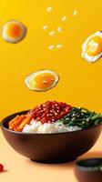 Bibimbap bowl with fried eggs floating, on yellow background. Food presentation concept photo