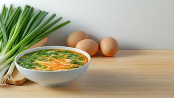 Bowl of soup with scallions on table, eggs next to it, simple light back. For food blog photo