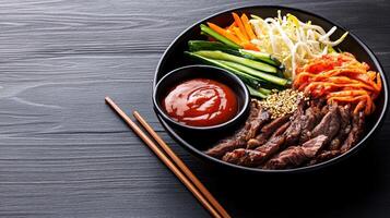 Bowl with beef strips and various vegetables and kimchi on a dark background. Possible use food blog photo